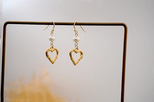 Detailed view of gold textured heart earrings with white freshwater pearls on a gold stand