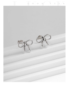 Macro detail of silver twisted bow stud earrings with vintage texture on white background