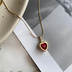 Macro detail of red heart zircon pendant on golden snake chain over a vintage magazine