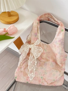 Pink floral tote bag with large white lace bow detail on a modern clear chair