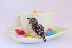 Detailed close-up of a golden bird keychain with black enamel and sparkling rhinestones