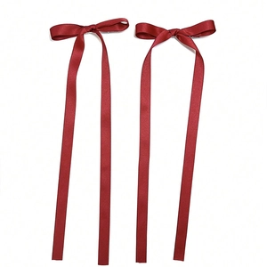 Close-up of a pair of red satin bow hair clips with long flowing ribbons on white background