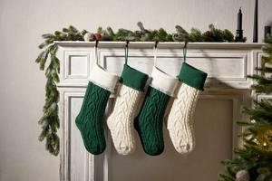 Knitted Christmas stockings with heart tassels hanging on a fireplace with pine cones