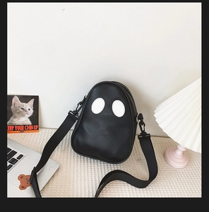 Detail of cute ghost-shaped black PU crossbody bag on a textured desk with lifestyle decor