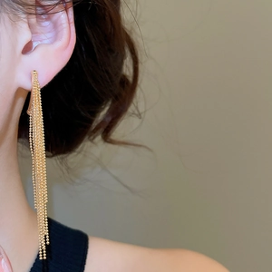 Detail shot of long gold ball chain tassel earrings worn by a model in a warm setting