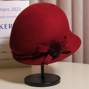 Close-up of elegant burgundy wool cloche hat with a bow and fluffy fur ball detail
