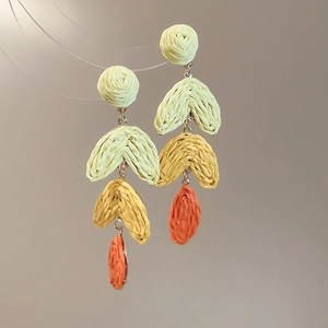 Macro detail of Bohemian raffia tassel earrings with three-color gradient woven texture