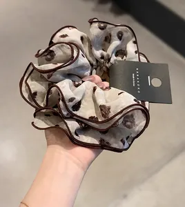 Detail of floral chiffon scrunchie with dark brown piping and authentic brand tag