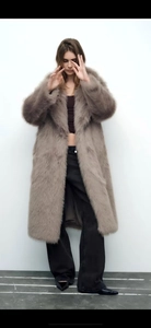 Detail of greyish-brown faux fur coat showing plush texture and long-line silhouette