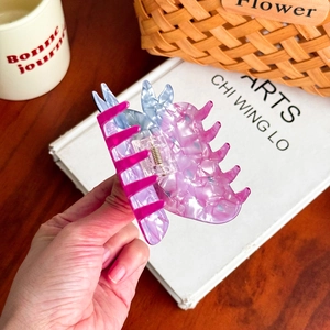 Hand holding a pink and blue gradient shark hair clip over a minimalist desk setup