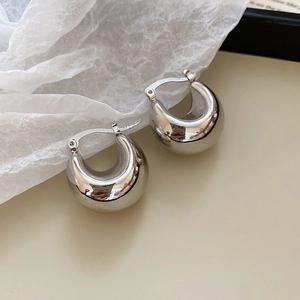 Macro shot of silver metallic geometric hoop earrings on textured beige background