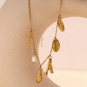Detailed view of an 18K gold plated necklace with seashell, pearl and letter A pendants