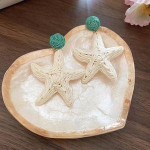 Detail view of woven raffia starfish earrings with green bead in a shell tray