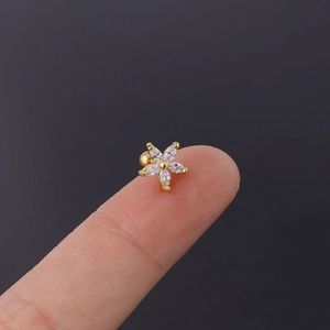 Detailed close-up of a tiny golden daisy earring with colorful zircons on a fingertip