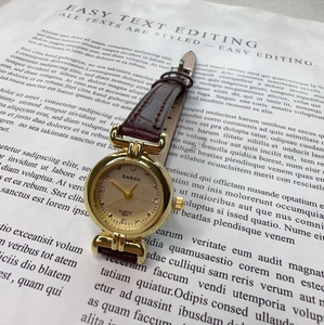 Detailed shot of retro women's quartz watch with gold case and brown leather strap on newsprint
