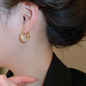 Close-up of sparkling gold C-shaped earrings with white zircons on a model's ear