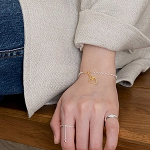 Elegant gold heart charm bracelet and silver rings worn on hand over soft linen fabric