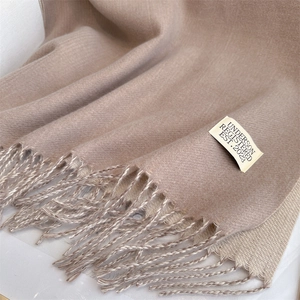 Detail of beige cashmere blend scarf showing brand tag and soft fringe texture