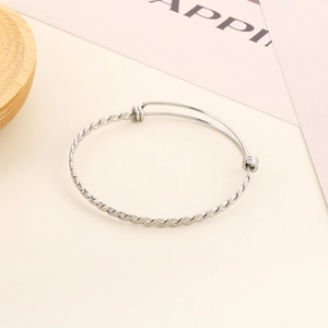 Macro detail of adjustable twisted silver stainless steel bangle on a minimalist background