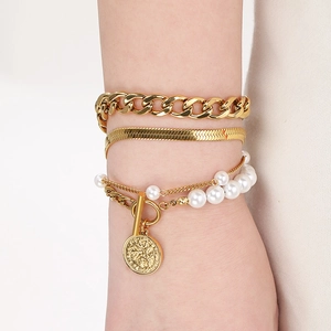 Detail of layered gold Cuban and snake chains with pearls and coin pendant on wrist