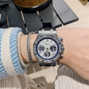 Close-up of a silver watch with a diamond bezel and black silicone strap on a wrist