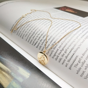 Elegant gold round pendant necklace with artistic female portrait line drawing on a book