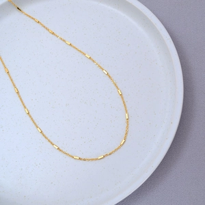 Detail of a minimalist gold-plated brass necklace with small cubes on a ceramic plate