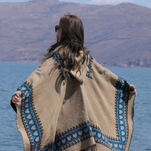Poncho à capuche ethnique camel avec motifs de cœurs bleus porté par un modèle au bord du lac