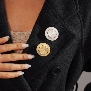 Metallic leather-wrapped round brooches with textured finish on black wool coat lapel