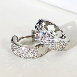 Vue macro de créoles argentées avec pavé de zircons et motifs de trèfles évidés