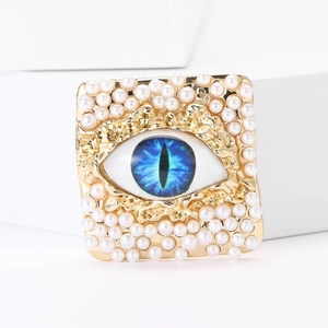 Macro detail of gold square brooch with blue evil eye motif and white pearls on edges