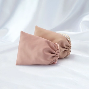 Detail of light pink and beige silk drawstring pouches for jewelry storage on satin background