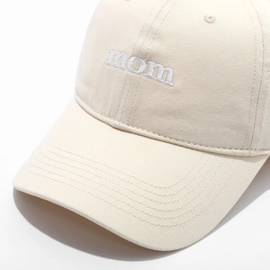Detailed view of white 'mom' embroidery on a cream cotton twill baseball cap