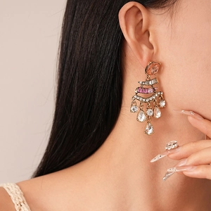 Macro detail of vintage gold earrings with pink rhinestone fringe worn by a model