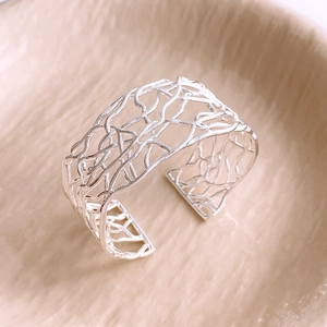 Detail of silver hollowed mesh open bangle on a textured beige ceramic plate