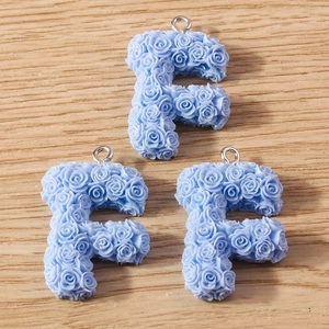 Macro detail of three light blue resin F-letter charms with 3D rose flower textures