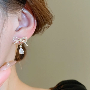 Detail of elegant gold bow earrings with imitation pearls and teardrop zircon on ear