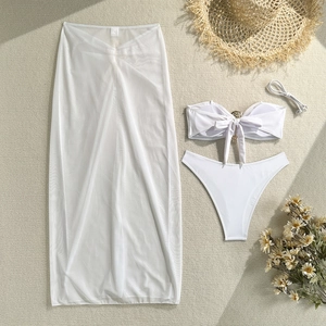 Flat lay of a white three-piece bikini set with a metal buckle and sheer mesh skirt