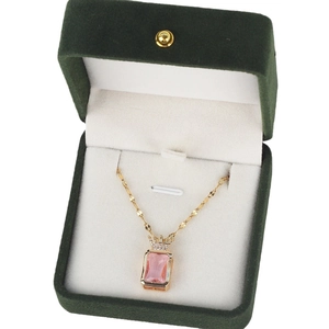 Elegant gold necklace with pink crystal and crown pendant in a green velvet jewelry box