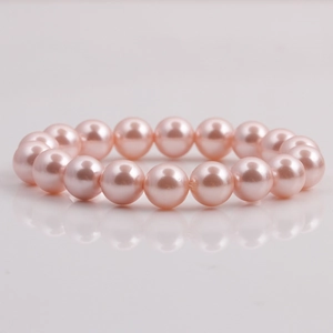 Macro detail of round 10mm pink shell pearls bracelet on a reflective white surface