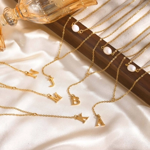 Detail view of golden Y-shaped initial necklaces with pearls on elegant silk fabric