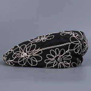 Detailed close-up of intricate white floral embroidery on a black breathable beret cap