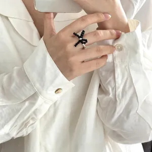 Detail of beaded ring featuring a black woven bow with a pearl center on a white band