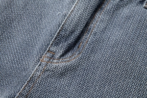 Macro shot of high-density herringbone denim fabric with orange double-stitching detail