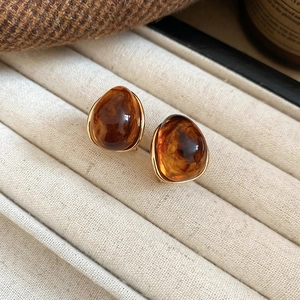 Close-up of golden brown resin earrings with gold metal edges in a beige jewelry box