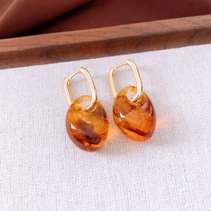 Detailed view of amber acrylic drop earrings with polished gold geometric hoops
