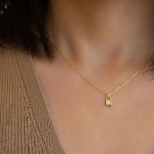 Close-up of a gold mini padlock pendant with a sparkling crystal on a model's neck
