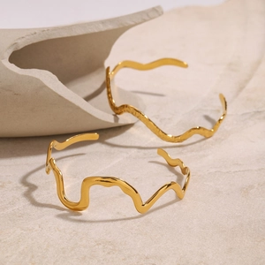 Gold wavy stainless steel bracelets featuring a liquid metal design on a stone pedestal