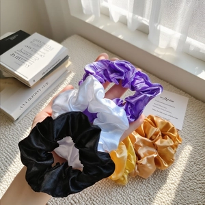 Assorted colorful satin scrunchies in purple, gold, and white held against a soft window light