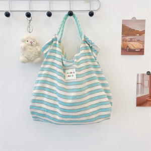 Detail of blue striped canvas tote bag with colorful logo patch and sheep plush charm